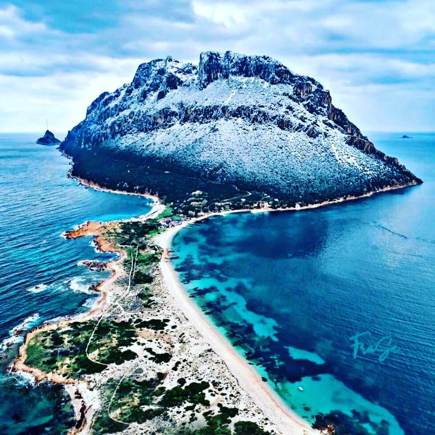 Vista aerea dell'isola di Tavolara con la vetta imbiancata di neve, una lingua di sabbia e il mare turchese